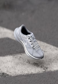 Graue Sportlaufschuhe mit einem Obermaterial aus Mesh, Schnürsystem und reflektierenden Akzenten, ausgestattet mit einer gepolsterten Sohle und einem schlanken Design.