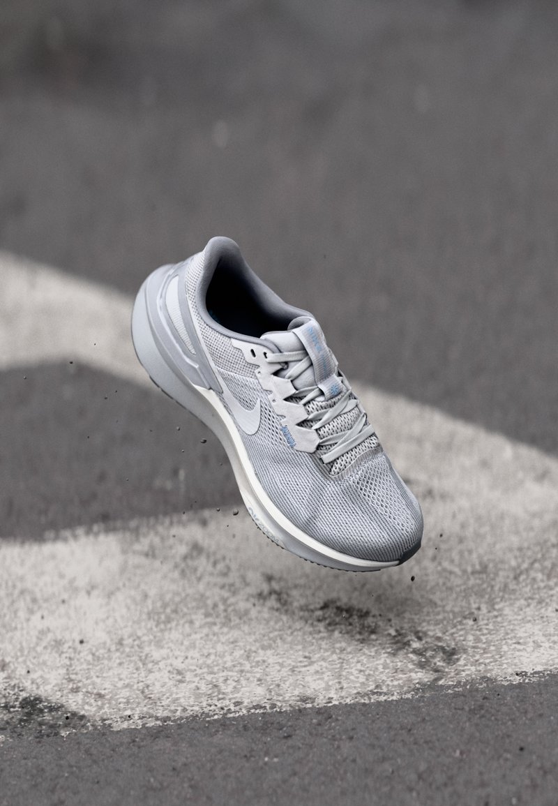 Graue Sportlaufschuhe mit einem Obermaterial aus Mesh, Schnürsystem und reflektierenden Akzenten, ausgestattet mit einer gepolsterten Sohle und einem schlanken Design.