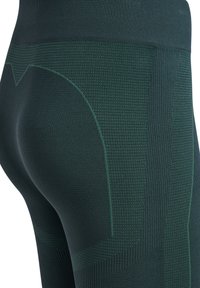 Nahaufnahme dunkelgrüner nahtloser, strukturierter Leggings, die Stoffmuster und Nähte im Hüft- und Oberschenkelbereich hervorheben.