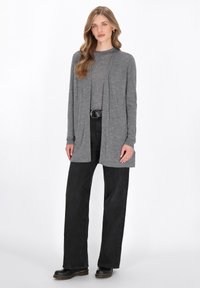 Cardigan grigio con apertura frontale, maniche lunghe e vestibilità comoda, indossato sopra un top grigio e abbinato a pantaloni neri a gamba larga e stivali.