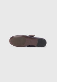 Sole di scarpa di un viola scuro con una texture liscia, caratterizzata da un accento in pelle marrone. Il tacco è arrotondato con una presa in gomma alla base.