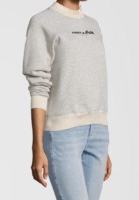 Sudadera gris claro con cuello y puños de canalé crema, que presenta el texto negro "ANDY & Pablo" en el frente. Material suave, corte relajado.