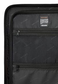 Interno di una borsa da viaggio nera, con tasche in rete, cerniere e un'etichetta. Tessuto liscio con branding tonale e cuciture durevoli.