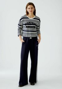 Gestreepte sweatshirt in marineblauw en wit met de tekst "BONJOUR AMOUR"; gecombineerd met marineblauwe trainingsbroek met zijstrepen en een trekkoord in de taille.