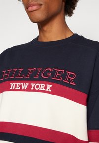 Felpa marina con strisce orizzontali rosse e bianche. Presenta il ricamo del testo "HILFIGER NEW YORK" e un design a collo rotondo.