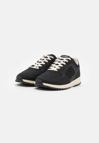 Svart sneakers med mesh-stoff og semsket skinn-detaller. Kremfargede snørebånd og såle. Lav profil design med strukturert overflate. Har merkevare på tungen.