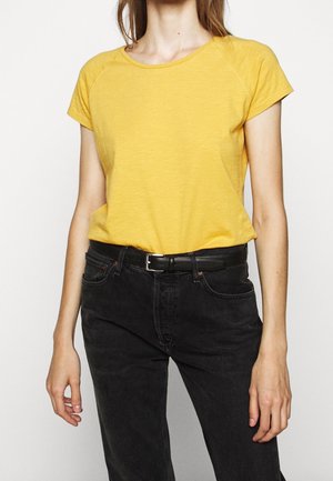 T-shirt jaune à manches courtes avec un col rond et des bordures côtelées, associé à un jean en denim noir taille haute et une fine ceinture noire.