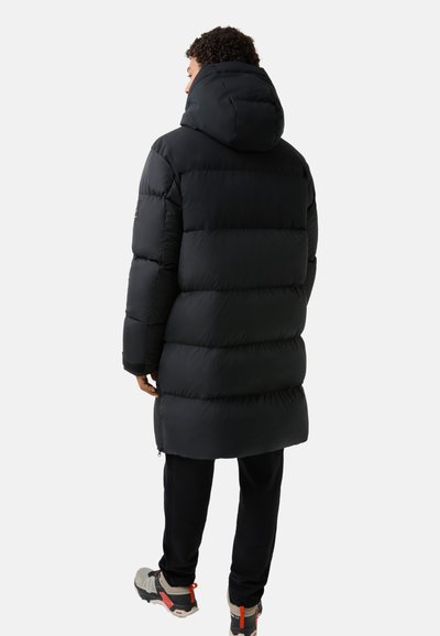 Schwarze Pufferjacke mit Kapuze, ausgestattet mit gestepptem Design und elastischen Bündchen; kombiniert mit schwarzen Hosen und grauen Schuhen, zeigt einen schlichten lässigen Stil.