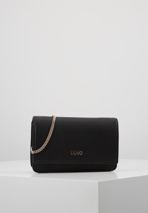Pochette en cuir noir texturé avec bandoulière chaîne dorée et logo Liu Jo doré sur le devant, posée sur un cube blanc sur fond uni.