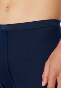 Boxers bleu marine en tissu doux. Ceinture texturée avec le nom de la marque subtilement embossé. Surface lisse avec des coutures minimales.