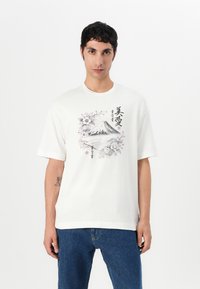 T-shirt en coton blanc avec un design graphique représentant une montagne et des fleurs dans des tons noirs et roses. Manches courtes et coupe décontractée.
