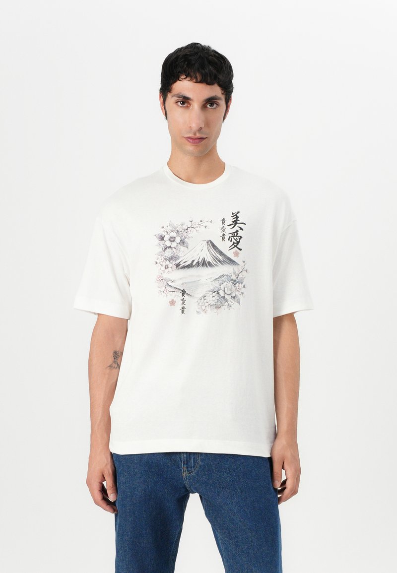 T-shirt en coton blanc avec un design graphique représentant une montagne et des fleurs dans des tons noirs et roses. Manches courtes et coupe décontractée.