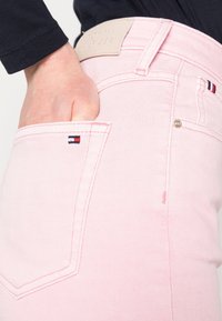 Jeans de mezclilla rosa con diseño de pierna recta, que presentan una etiqueta con el logo de Tommy Hilfiger en la cinturilla y un pequeño detalle del logo cerca del bolsillo.
