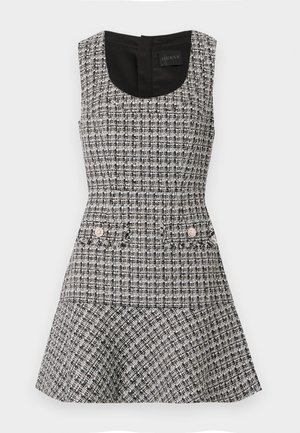 Sleeveless dress in black and white tweed with a fitted bodice, flared skirt, and two front pockets adorned with round embellishments.