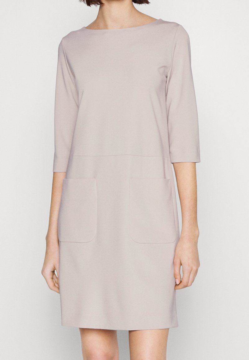 Ljusrosa klänning med rund halsringning, trekvartsärmar och två stora framfickor. Slät textur och rak silhuett.