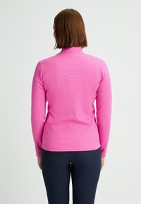 Långärmad, rosa atletisk topp med hög krage och strukturerad tyg, matchad med mörka, åtsittande leggings.