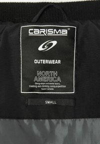 Schwarzes Stoffetikett mit weißem Text. Markenname "CARISMA" oben, gefolgt von "OUTERWEAR", "NORTH AMERICA" und der Größe "SMALL" am unteren Ende.