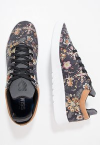 Baskets noires texturées avec un imprimé floral multicolore, dotées d'une semelle blanche, d'accents gris et de lacets noirs.