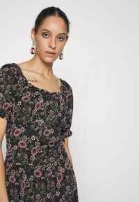 Vestido preto floral com mangas bufantes, apresentando padrões de flores rosa e verdes e um decote quadrado. Detalhe de botão marrom na cintura.