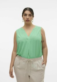 Mintgrøn ærmeløs bluse med V-hals og tekstureret stof, parret med beige bukser med elastisk liv og lommer.