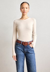 Ribbed beige long-sleeve top paired with high-waisted blue denim jeans. Brown braided belt with a circular buckle accentuates the waist.