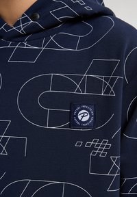 Sudadera azul marino con patrones geométricos blancos, tejido suave, gran bolsillo canguro y un parche con logotipo y marca en el lado izquierdo del pecho.