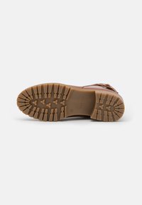 Bota de cuero marrón con una suela texturizada que presenta surcos profundos y un patrón en zigzag para tracción. Incluye un detalle decorativo de hebilla.