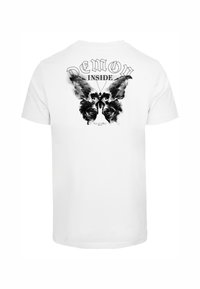 Hvit bomull T-skjorte med et svart grafisk design av en sommerfugl og hodeskaller med teksten "DEMON INSIDE" over.