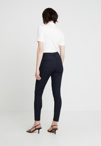 Svarta figurnära byxor i stretchmaterial, med en platt midja, bakfickor och en elegant ankellängd. I kombination med en vit topp.