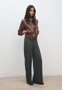 Brun lädercroppad bomberjacka med ribbade muddar, kombinerad med vida, mörkgröna byxor och en figursydd topp med bältesdetalj.