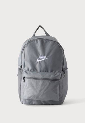 Grå Nike rygsæk med hvidt logo, lomme med lynlås foran, øverste håndtag og sidelomme i net på en ensartet hvid baggrund.