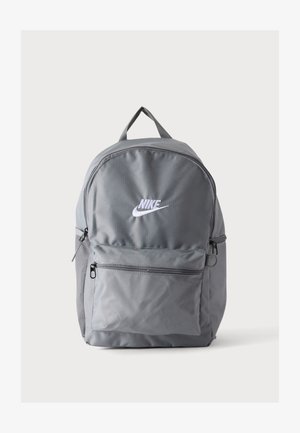 Szary plecak Nike z białym logo, przednią kieszenią na zamek, górnym uchwytem i boczną kieszenią z siatki na jednolitym białym tle.