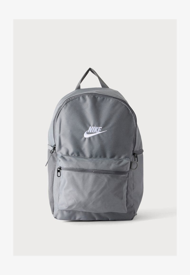 Γκρι σακίδιο Nike με λογότυπο σε λευκό, μπροστινή τσέπη με φερμουάρ, επάνω χερούλι και πλαϊνή τσέπη από δίχτυ σε απλό λευκό φόντο.