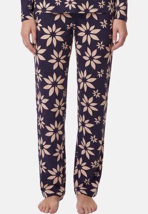 Marineblaue Pyjamahose mit großem beigen Blumenmuster, getragen von einer Person, die barfuß steht und die Hände entspannt an den Seiten hängen lässt.