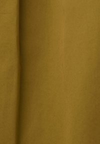 Gros plan d’un tissu jaune moutarde avec une texture de tissage diagonal visible et de légères plis en ombre.