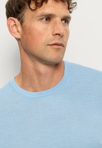 Hellblau gestreiftes Kurzarm-T-Shirt mit Rundhalsausschnitt, aus weichem Stoff, mit glatter Textur und minimalistischem Design.