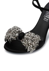 Sandal con tacco nero e tomaia in tessuto testurizzato, caratterizzata da un grande fiocco decorativo in paillettes argento sulla fascia delle dita e da una sottile cinghia alla caviglia.