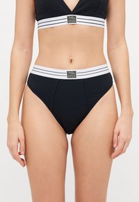 Svart bomullsundertøysett med bralette med V-hals og høyde midje truser. Inkluderer hvite stripete elastiske bånd med logo detaljer.