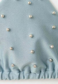 Tissu bleu clair avec une couture froncée et de petites perles argentées cousues uniformément sur la surface.