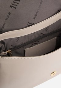 Interno di borsa in pelle beige con fodera grigia, dotato di una tasca con cerniera e di uno scomparto per carte, logo in rilievo visibile sulla tasca.