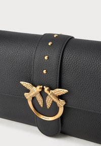 Clutch in pelle nera texture con una chiusura a forma di uccello dorato e piccoli chiodini dorati sulla chiusura della tracolla.