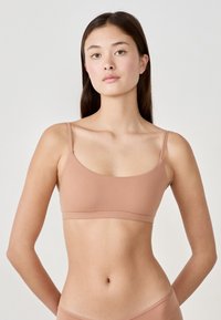 Reggiseno stile bandeau in marrone chiaro, realizzato in tessuto morbido. Presenta spalline sottili regolabili e un design senza cuciture privo di decorazioni.