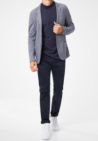 Šedý kostkovaný blazer přes tmavě modré tričko, spárovaný s úzkými modrými kalhotami a bílými teniskami. Blazer má dvě přední kapsy a detail na klopě.