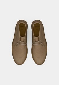 Ζευγάρι μπεζ σουέντ desert μπότες με κορδόνια, άνω όψη, με την ένδειξη "BOSS" μέσα σε κάθε παπούτσι.