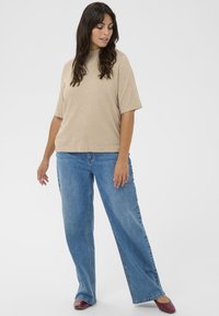 Beige top med korte ærmer og høj hals, kombineret med lyseblå viddebukser og bordeaux spidse flade sko. Glat stof og afslappet pasform.