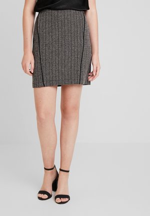 Kobieta w czarno-białej teksturowanej mini spódnicy z czarnymi pionowymi paskami, w połączeniu z czarnymi sandałami na słupku z paskiem wokół kostki.