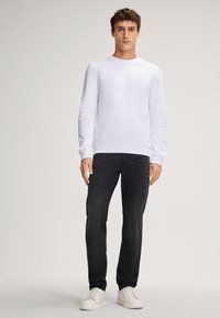 Felpa bianca con maniche lunghe e collo rotondo; abbinata a jeans scuri e sneakers bianche. Tessuto liscio, design aderente.