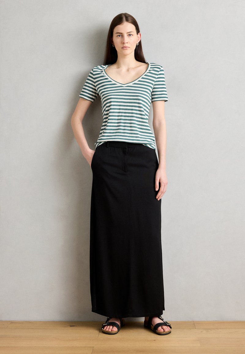 Pasiasty zielono-biały top z krótkim rękawem, czarna spódnica maxi i czarne sandały. Gładki materiał o luźnym kroju, z dekoltem w kształcie litery V.