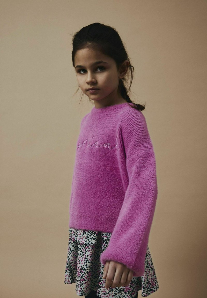 Maglione rosa fluffy con maniche lunghe e testo ricamato, abbinato a una gonna con un motivo animalier multicolore.