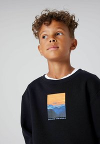 Crna dukserica s pravokutnim grafičkim prikazom planina pri zalasku sunca, s natpisom "ISTRAŽITE SVIJET" u bijelom na dnu.